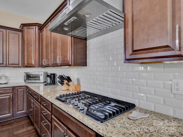 kitchen with backsplash, stainless steel gas stovetop, dark wood-type flooring, wall chimney exhaust hood, and light stone counters