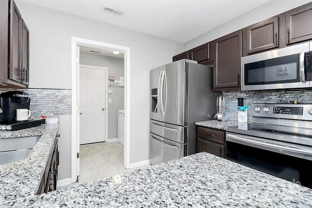 kitchen featuring dark brown cabinetry, light stone countertops, stainless steel appliances, and tasteful backsplash