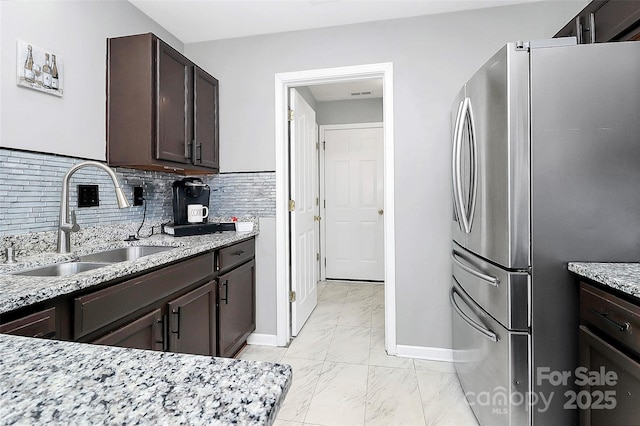 kitchen featuring light stone countertops, sink, stainless steel fridge, decorative backsplash, and dark brown cabinets