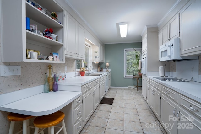 kitchen featuring white appliances, white cabinets, a kitchen breakfast bar, sink, and crown molding