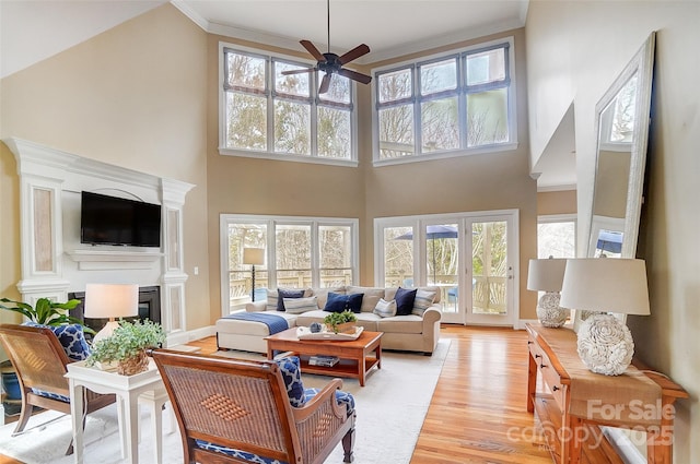 living room with crown molding, a towering ceiling, ceiling fan, and light wood-type flooring