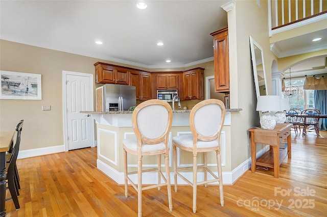 kitchen featuring light hardwood / wood-style flooring, a kitchen breakfast bar, stainless steel appliances, light stone counters, and kitchen peninsula