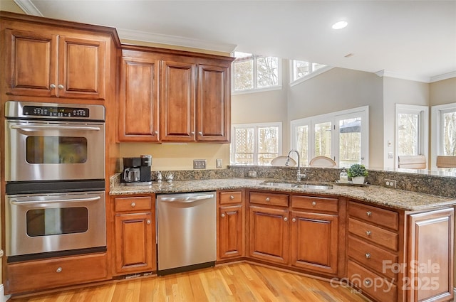 kitchen with appliances with stainless steel finishes, plenty of natural light, sink, ornamental molding, and light stone countertops