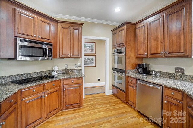 kitchen with crown molding, appliances with stainless steel finishes, dark stone countertops, and light hardwood / wood-style floors