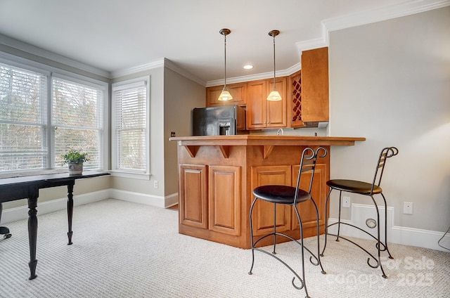 kitchen featuring a kitchen bar, black fridge, crown molding, decorative light fixtures, and kitchen peninsula