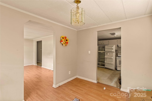 spare room featuring wood-type flooring, crown molding, and a notable chandelier