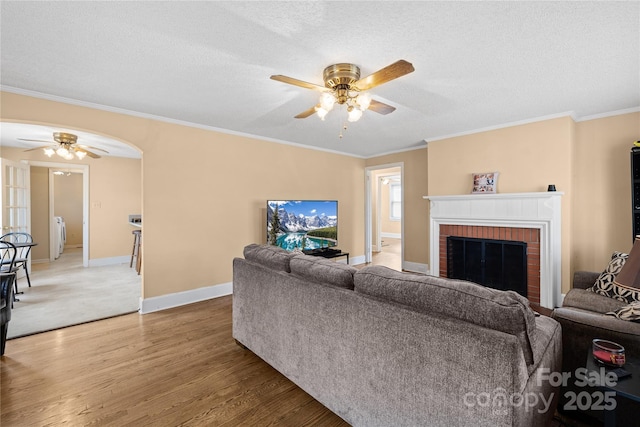 living room featuring ornamental molding, hardwood / wood-style floors, a textured ceiling, and a brick fireplace