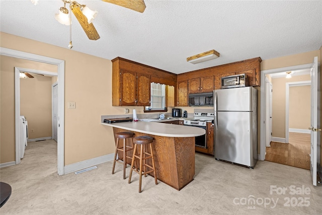 kitchen with appliances with stainless steel finishes, kitchen peninsula, ceiling fan, a breakfast bar, and a textured ceiling