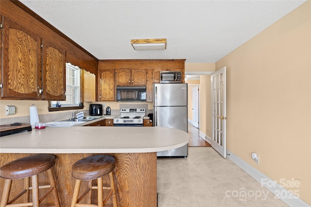 kitchen featuring kitchen peninsula, a textured ceiling, appliances with stainless steel finishes, and a kitchen breakfast bar