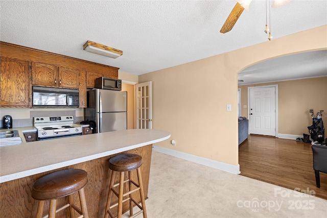 kitchen with a breakfast bar area, appliances with stainless steel finishes, ceiling fan, a textured ceiling, and sink