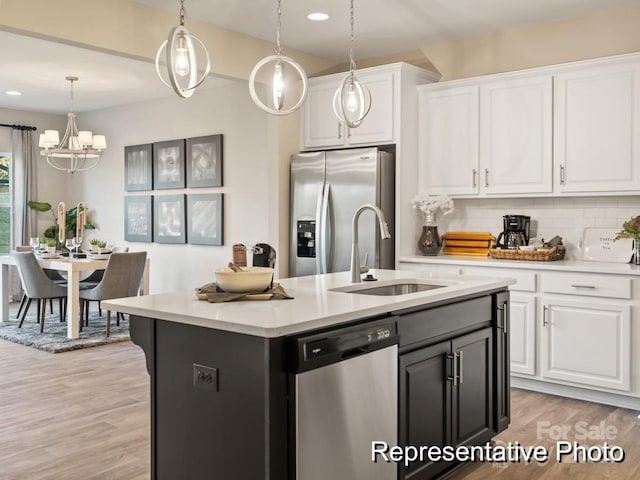 kitchen with stainless steel appliances, sink, decorative light fixtures, white cabinetry, and an island with sink