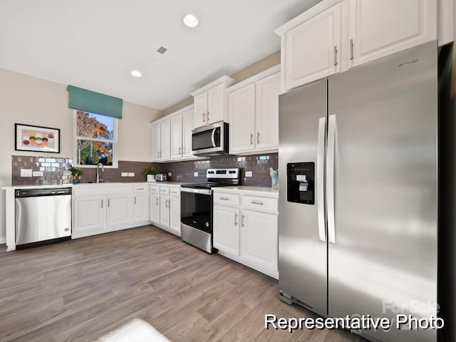 kitchen featuring stainless steel appliances, white cabinetry, and light hardwood / wood-style floors