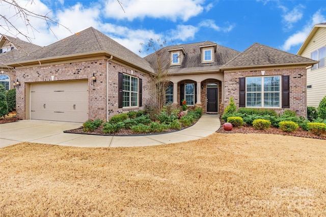 view of front facade featuring brick siding, a shingled roof, concrete driveway, an attached garage, and a front yard