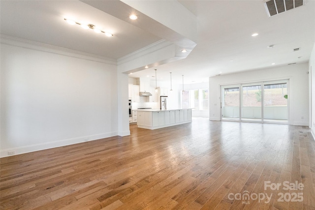 unfurnished living room featuring light wood finished floors, baseboards, visible vents, crown molding, and recessed lighting