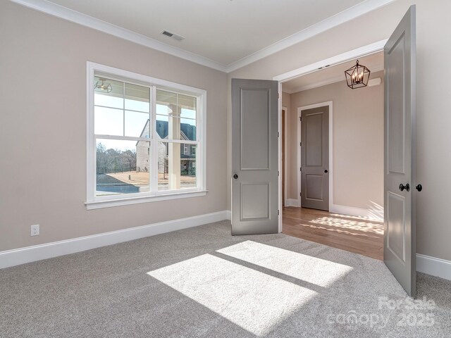 unfurnished room featuring a chandelier, carpet flooring, visible vents, baseboards, and crown molding