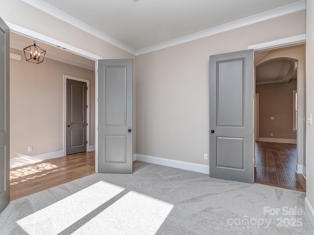 carpeted empty room with baseboards, arched walkways, ornamental molding, wood finished floors, and a notable chandelier