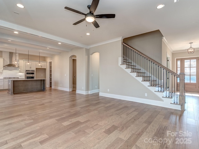 unfurnished living room featuring baseboards, arched walkways, ornamental molding, stairs, and light wood-style floors