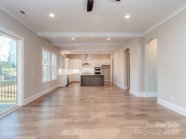 kitchen featuring light wood-style floors, arched walkways, a sink, and wall chimney exhaust hood