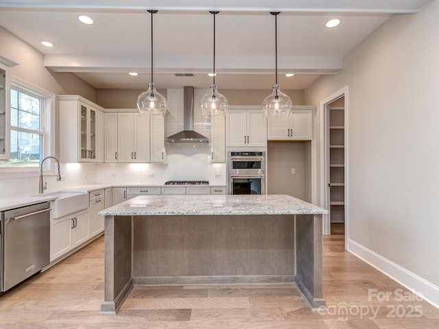 kitchen featuring a center island, stainless steel appliances, decorative backsplash, a sink, and wall chimney range hood