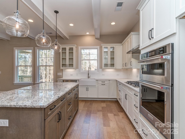 kitchen with visible vents, decorative backsplash, beamed ceiling, light wood-style floors, and a sink