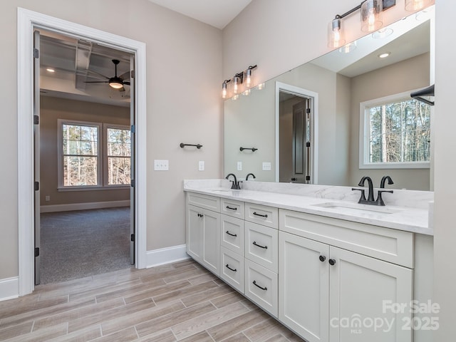 full bath featuring wood tiled floor, a sink, baseboards, and double vanity