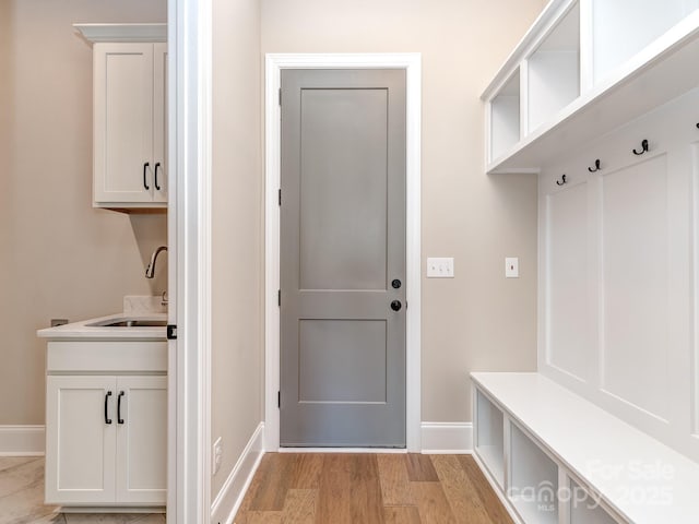 mudroom featuring baseboards, a sink, and light wood finished floors