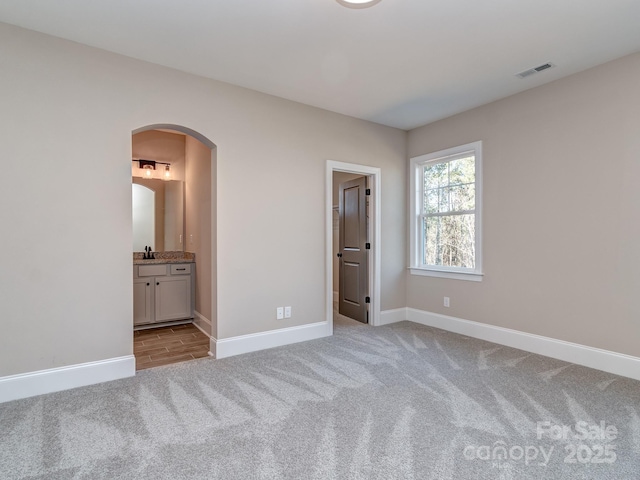 unfurnished bedroom with baseboards, visible vents, arched walkways, and light colored carpet