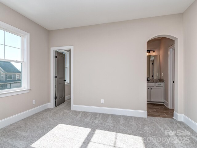 unfurnished bedroom featuring arched walkways, carpet, ensuite bathroom, and baseboards