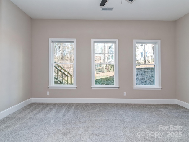 carpeted empty room with plenty of natural light, visible vents, ceiling fan, and baseboards