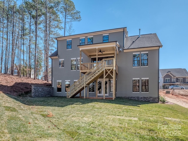 rear view of property with a deck, a ceiling fan, stairs, roof with shingles, and a lawn