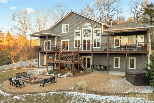 snow covered house with a wooden deck, a hot tub, a fire pit, and a patio