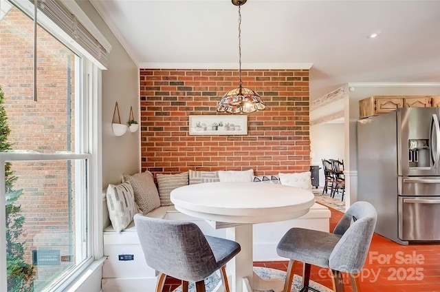 dining room featuring breakfast area, an accent wall, brick wall, and crown molding