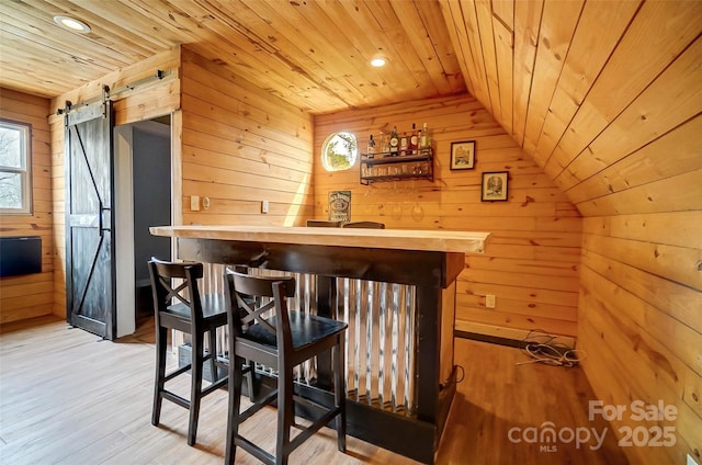 bar with a barn door, wooden walls, wooden ceiling, and light wood finished floors