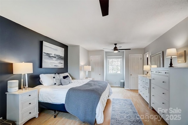 bedroom with baseboards, light wood-style flooring, two closets, and a ceiling fan