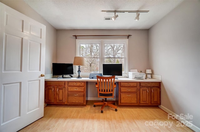 office space featuring baseboards, visible vents, a textured ceiling, and light wood-style floors