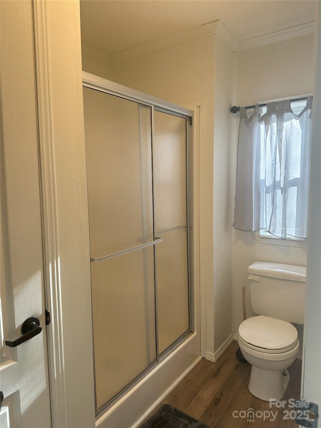 bathroom featuring crown molding, a shower with shower door, toilet, and wood-type flooring