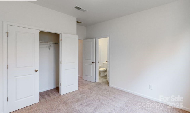 unfurnished bedroom with light colored carpet, a closet, and ensuite bathroom