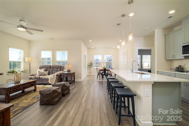 kitchen with decorative light fixtures, ceiling fan, sink, a kitchen island with sink, and hardwood / wood-style flooring