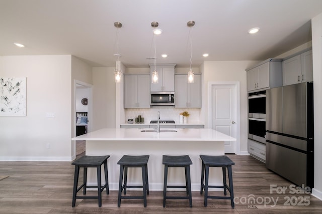 kitchen with appliances with stainless steel finishes, sink, backsplash, hanging light fixtures, and a kitchen island with sink