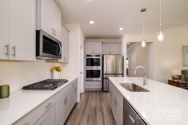 kitchen with appliances with stainless steel finishes, wood-type flooring, tasteful backsplash, sink, and hanging light fixtures