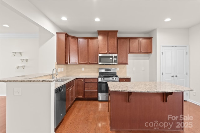 kitchen with light stone countertops, light wood-type flooring, appliances with stainless steel finishes, a kitchen breakfast bar, and sink