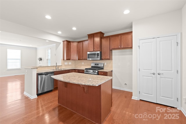 kitchen featuring sink, light stone counters, light hardwood / wood-style flooring, kitchen peninsula, and appliances with stainless steel finishes