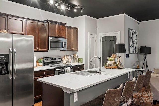 kitchen with stainless steel appliances, an island with sink, sink, a breakfast bar, and dark brown cabinets