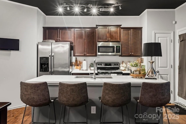 kitchen featuring dark brown cabinets, hardwood / wood-style flooring, stainless steel appliances, and a center island with sink