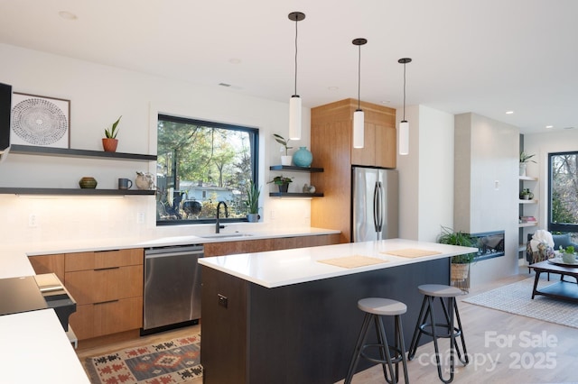 kitchen with sink, stainless steel appliances, light wood-type flooring, and hanging light fixtures