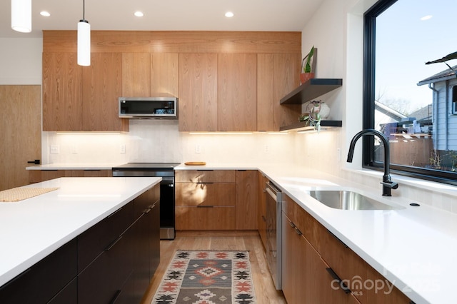 kitchen with sink, stainless steel appliances, light hardwood / wood-style floors, and decorative light fixtures