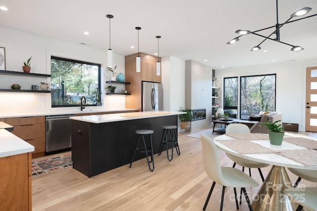 kitchen with a chandelier, appliances with stainless steel finishes, hanging light fixtures, a kitchen island, and light hardwood / wood-style flooring