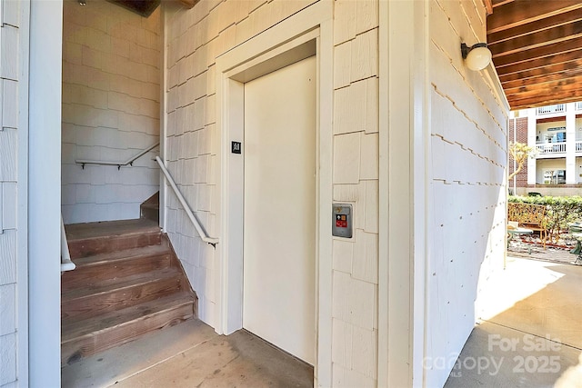 stairs featuring elevator and concrete flooring