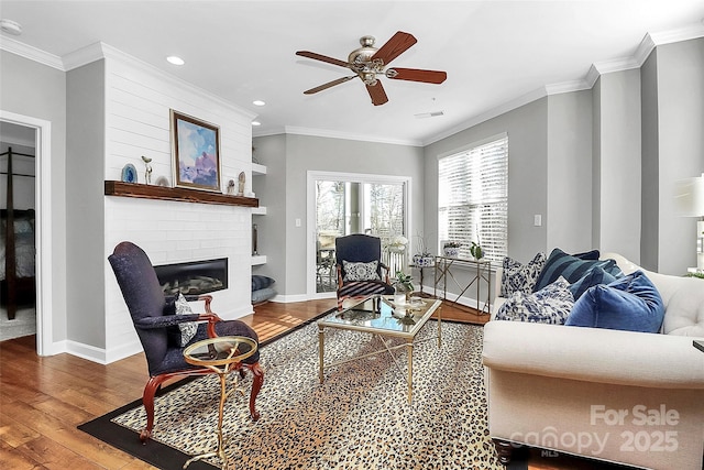 living room with a brick fireplace, ceiling fan, hardwood / wood-style flooring, and crown molding