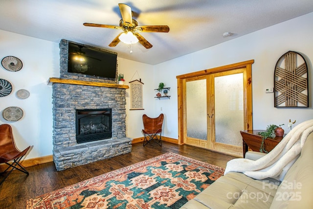 living room featuring a stone fireplace, dark wood-type flooring, a textured ceiling, and ceiling fan